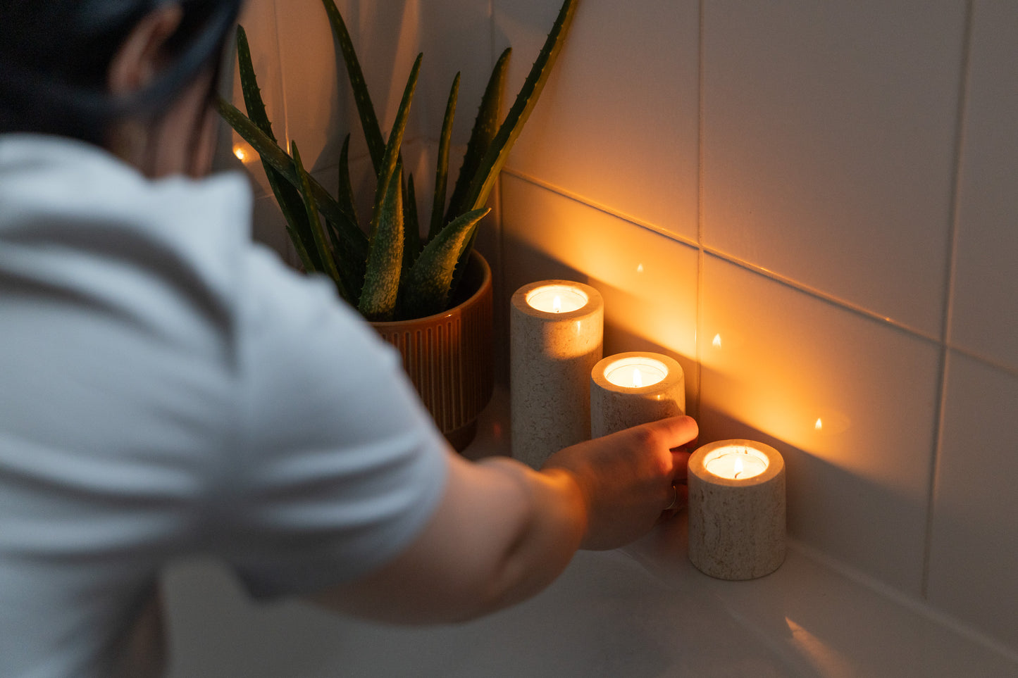 Luxuriöse Spa-Ambiente-Aufnahme im Badezimmer, bei der das dreiteilige Travertin-Teelichthalter-Set von Marmonix stimmungsvoll am Rand einer Badewanne angezündet wird, um eine entspannende Wellness-Atmosphäre zu kreieren.