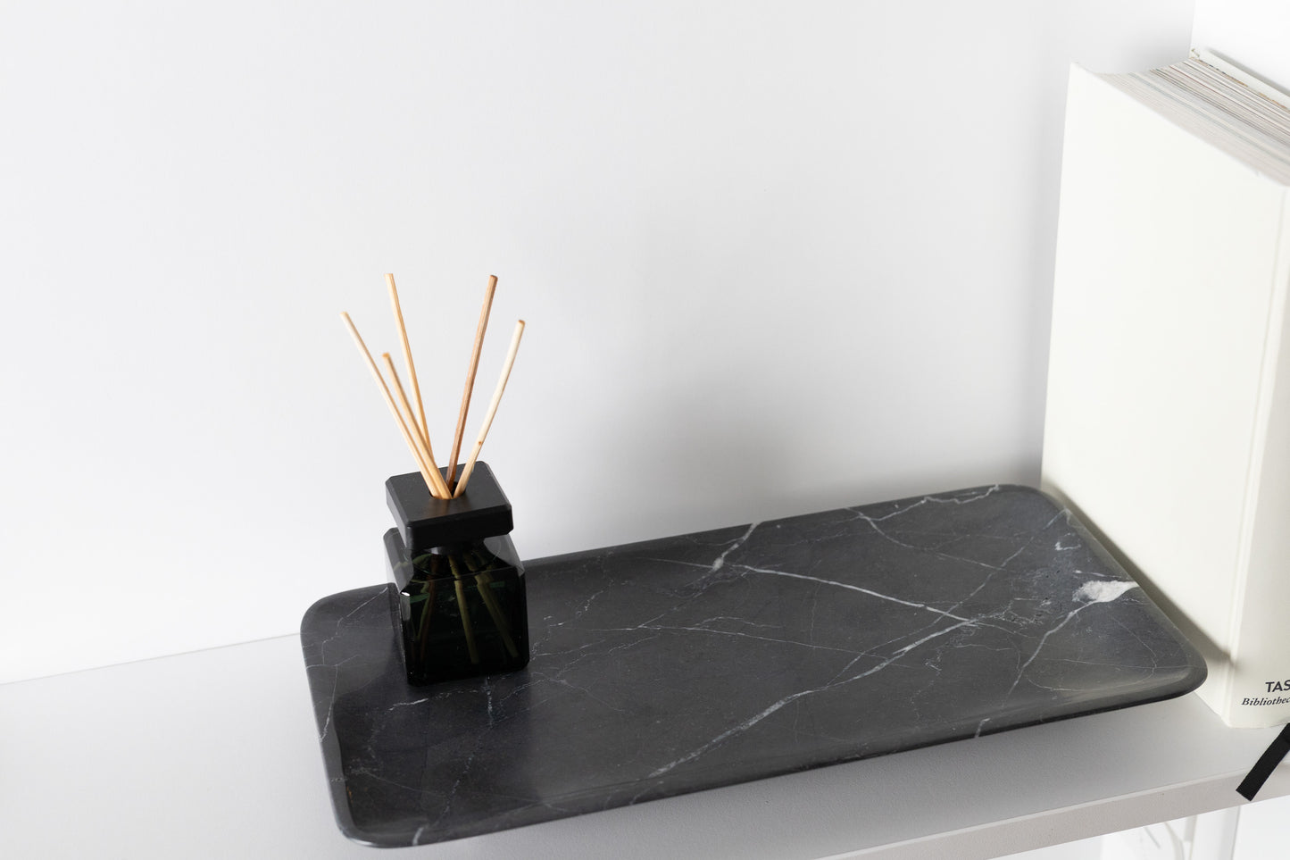 Exklusive und besonders luxuriöse Ambient-Aufnahme des 30x15 cm großen schwarzen Marmortabletts von Marmonix, kunstvoll arrangiert auf einem edlen Sideboard neben einem Buch für ein anspruchsvolles Interieur-Design.