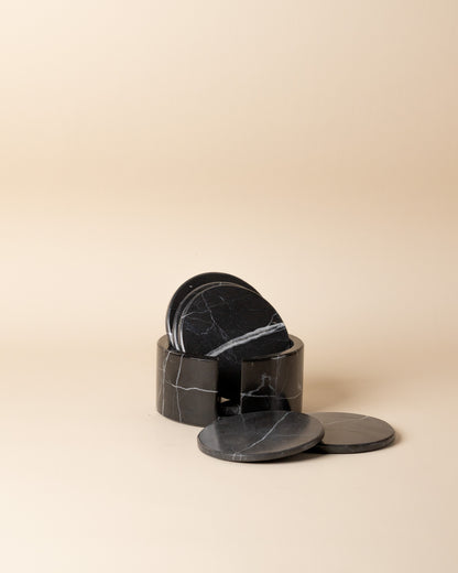 Set of black marble coasters with a holder on a beige background