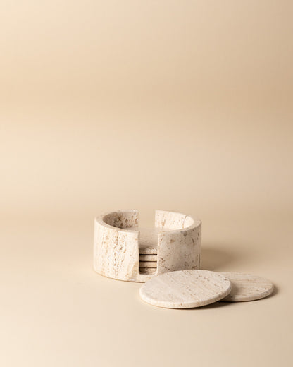 Set of travertine marble coasters with a holder on a beige background