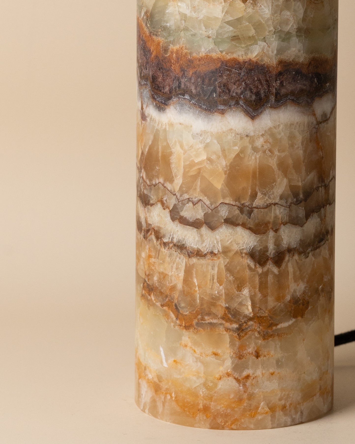 Cylindrical stone lamp with layered rainbow onyx pattern on a beige background