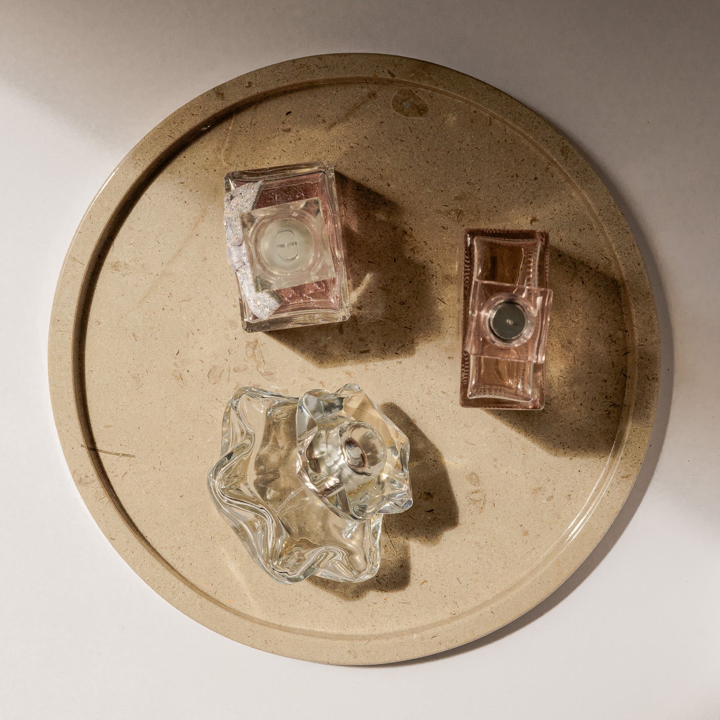 Kunstvolle Ambient-Aufnahme des runden Travertin-Tabletts von Marmonix, edel inszeniert mit exklusiven Parfümflakons und eleganten Licht- und Schattenspielen auf einem modernen Frisiertisch.