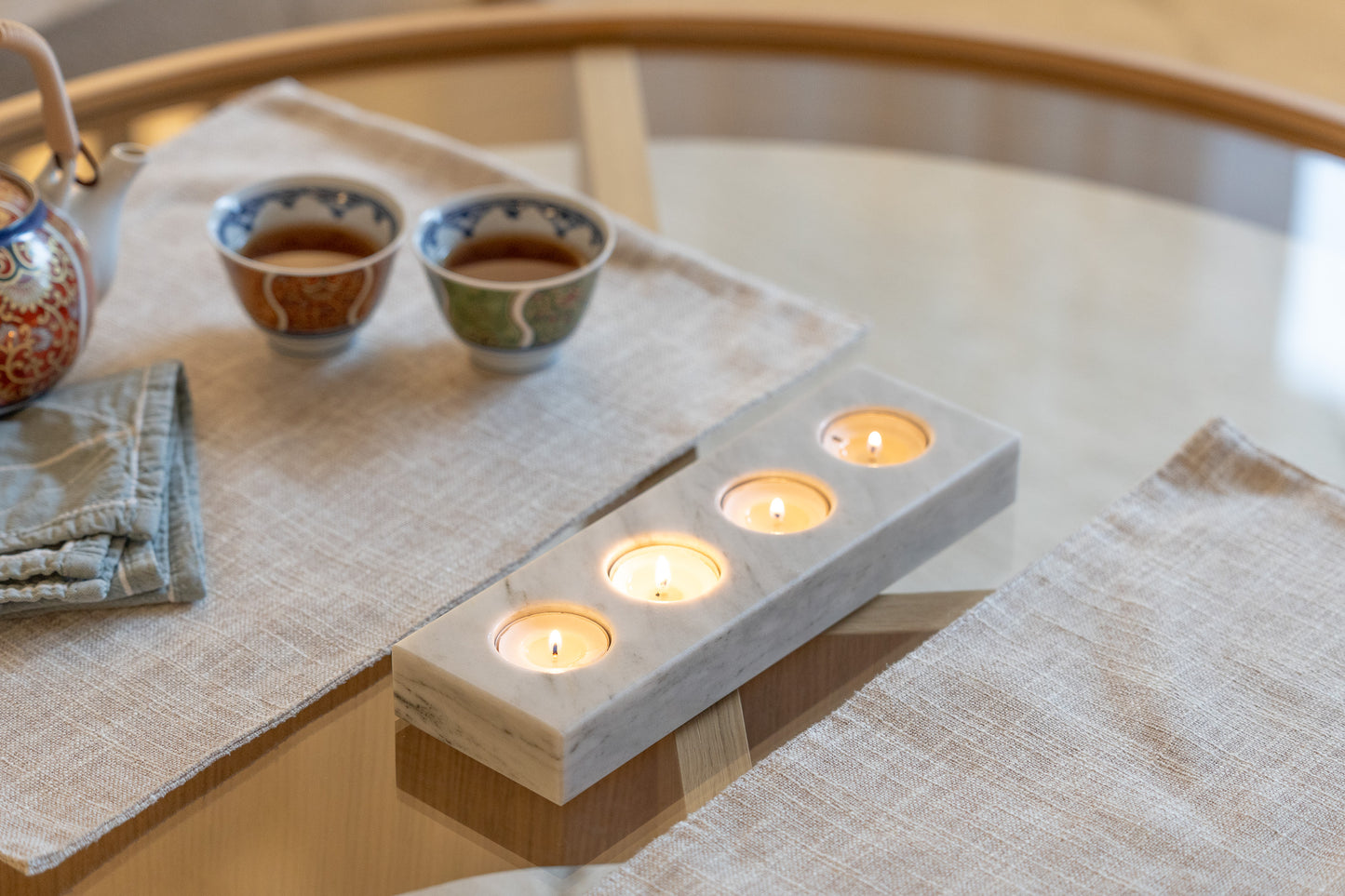 Elegante Ambiente-Aufnahme des vierteiligen Teelichthalters aus weißem Marmor von Marmonix, stilvoll platziert auf einem modernen Glastisch neben feinen Teetassen für ein luxuriöses und einladendes Design-Erlebnis im Wohnbereich.