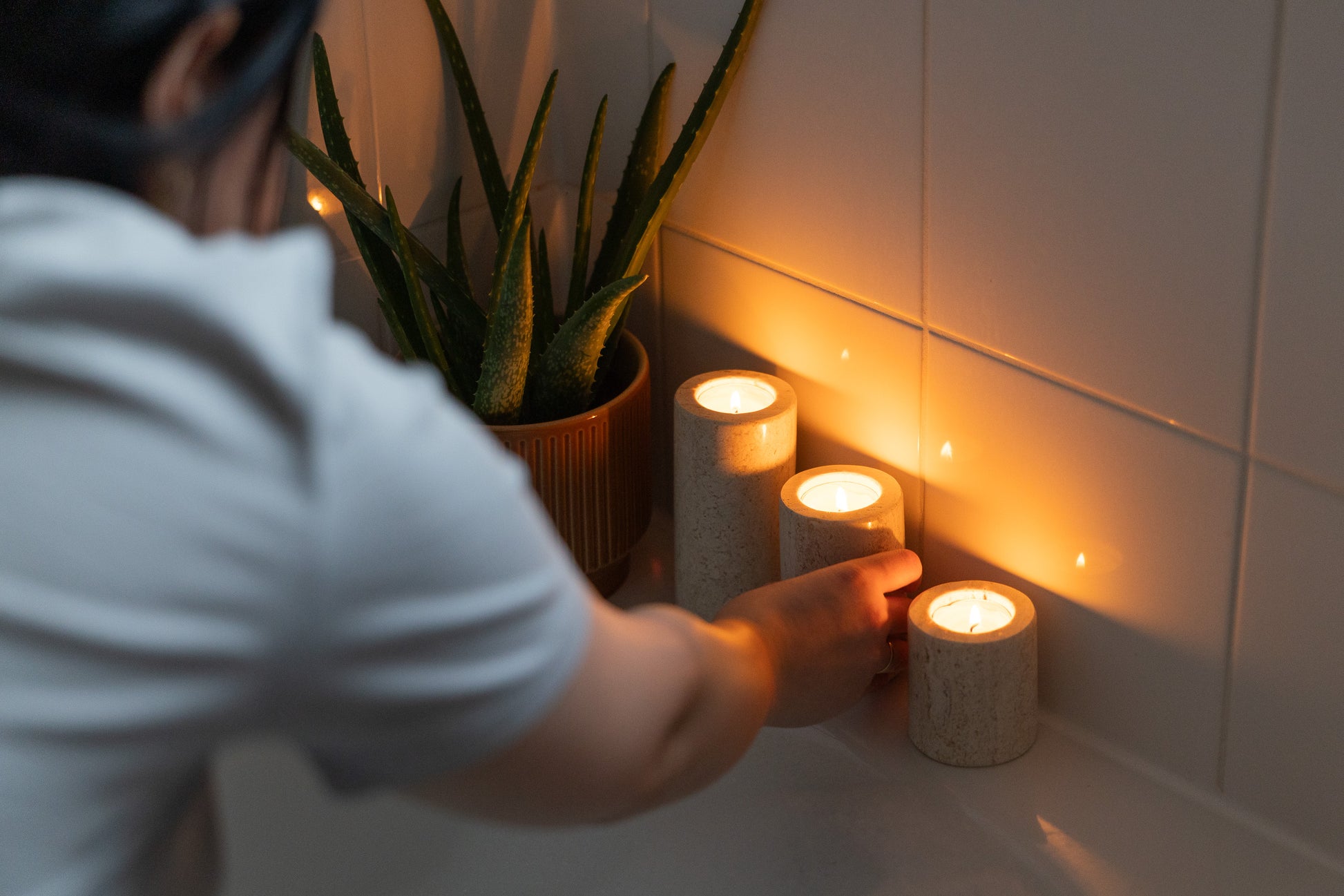 Luxuriöse Spa-Ambiente-Aufnahme im Badezimmer, bei der das dreiteilige Travertin-Teelichthalter-Set von Marmonix stimmungsvoll am Rand einer Badewanne angezündet wird, um eine entspannende Wellness-Atmosphäre zu kreieren.