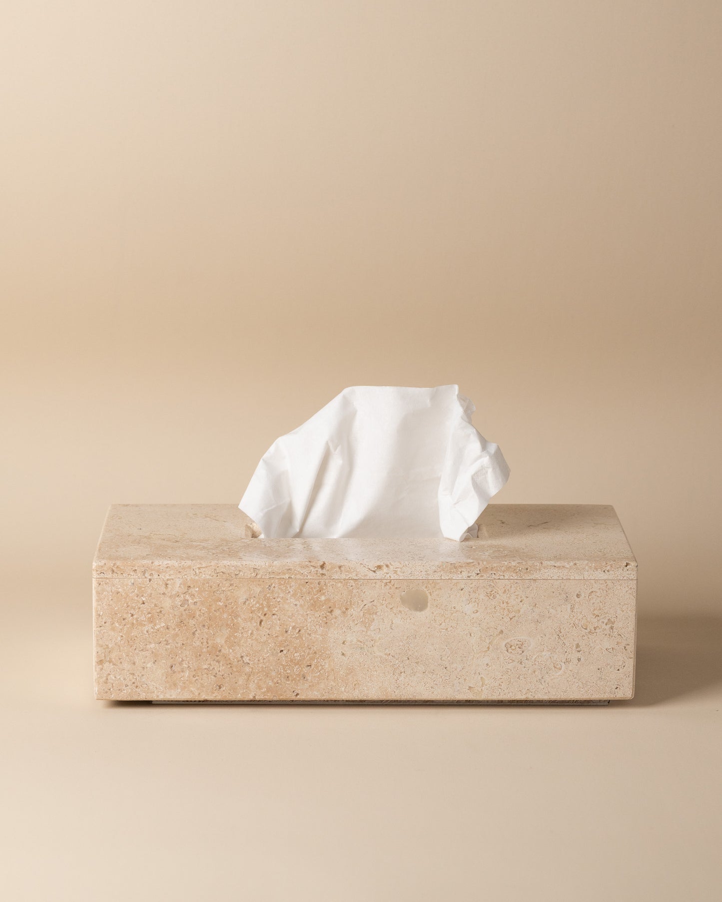 Travertine tissue box with a tissue peeking out on a beige background