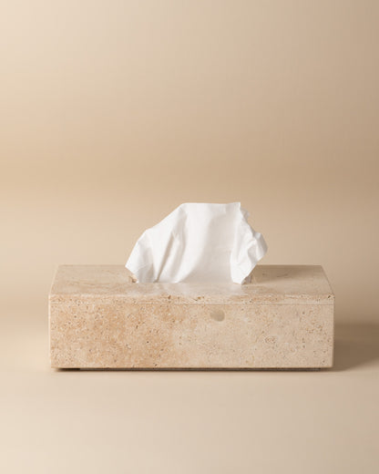Travertine tissue box with a tissue peeking out on a beige background