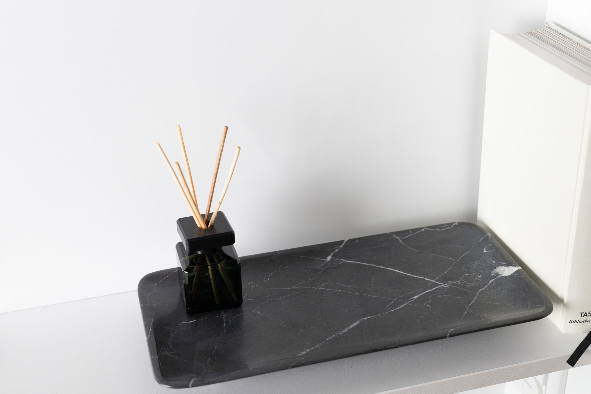 Exklusive und besonders luxuriöse Ambient-Aufnahme des 30x15 cm großen schwarzen Marmortabletts von Marmonix, kunstvoll arrangiert auf einem edlen Sideboard neben einem Buch für ein anspruchsvolles Interieur-Design.