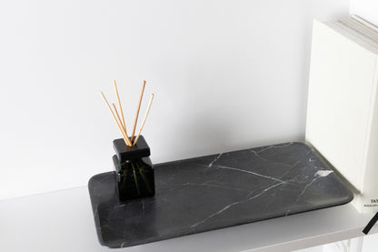 Exklusive und besonders luxuriöse Ambient-Aufnahme des 30x15 cm großen schwarzen Marmortabletts von Marmonix, kunstvoll arrangiert auf einem edlen Sideboard neben einem Buch für ein anspruchsvolles Interieur-Design.